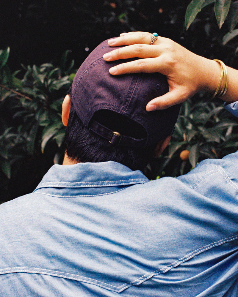 Person wearing a purple cap and blue shirt with greenery in the background