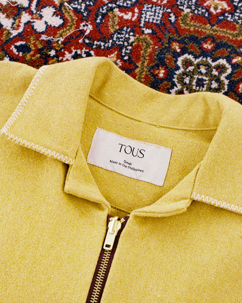 Yellow canvas jacket with a Tous label against a patterned rug background