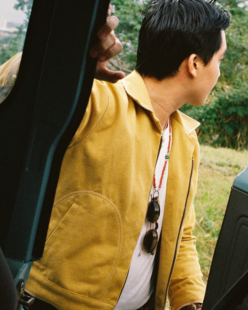 Person wearing a yellow jacket with sunglasses hanging from their collar, standing outdoors.