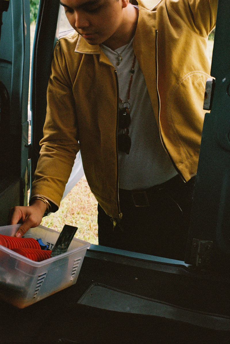 Person in a yellow canvas jacket reaching into a container next to an open car door of a vintage 1960 Toyota Landcruiser