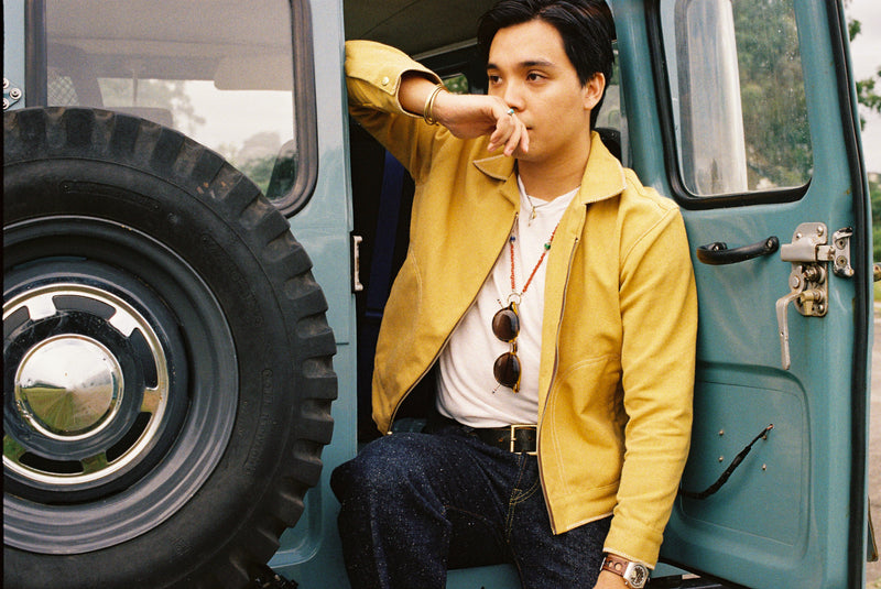 Man in a canvas yellow tous jacket sitting on the back of a vintage 1960 Toyota Landcruiser