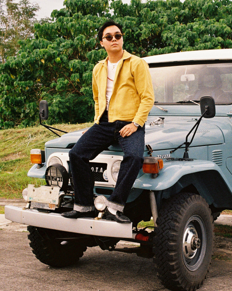 Person sitting on a vintage light blue truck in a natural setting wearing a canvas cropped jacket