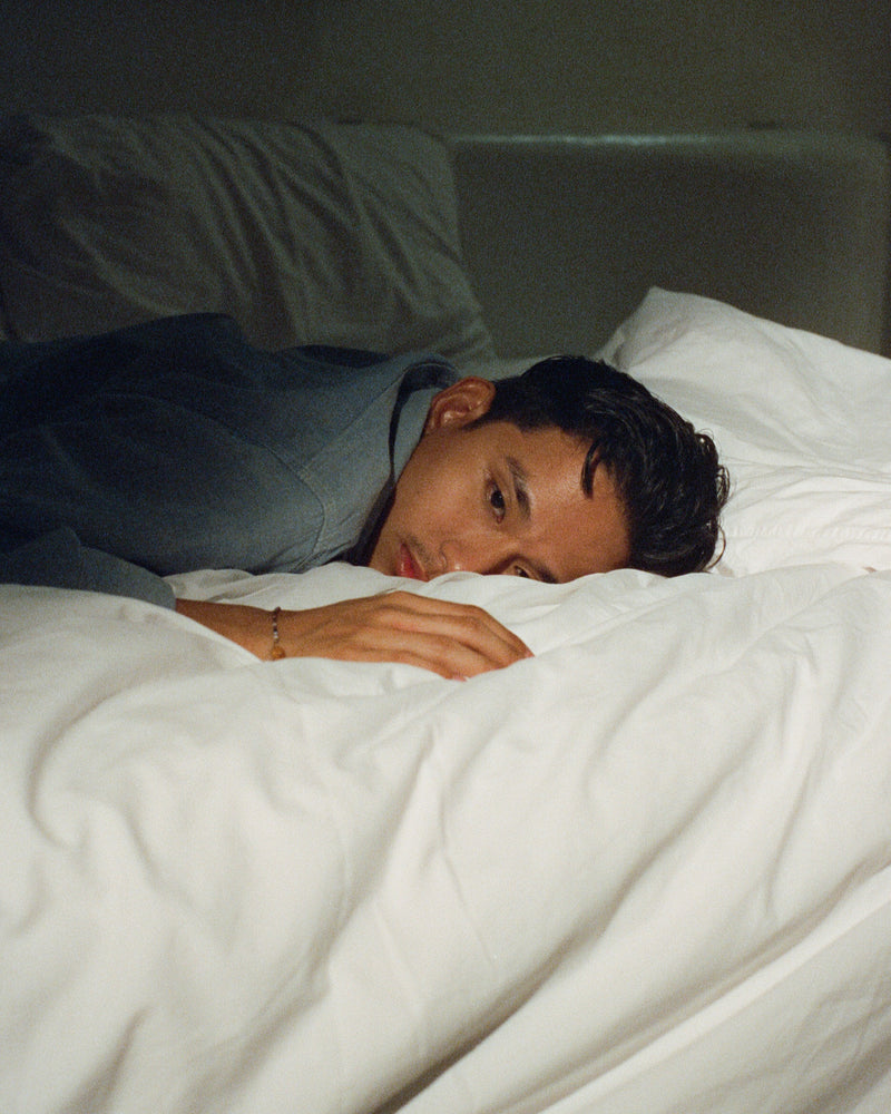 Person lying in bed under white sheets in a dimly lit room