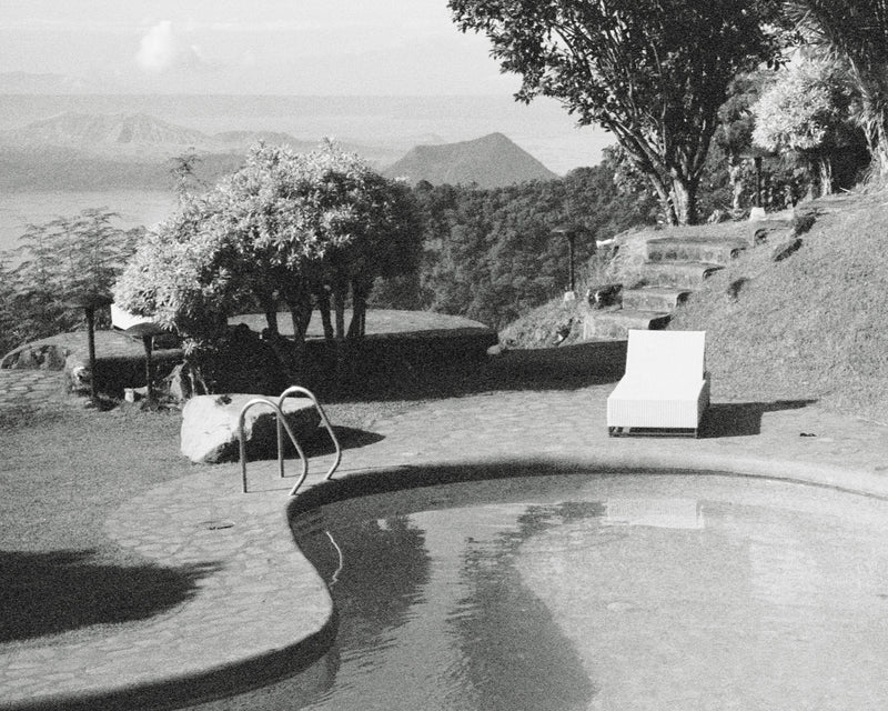 Black and white image of a pool area with lounge chairs and trees.