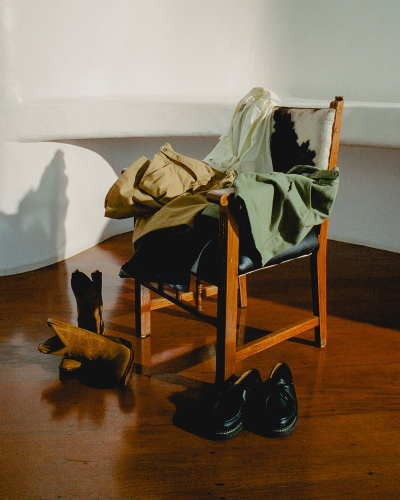 Chair with clothes draped over it on a wooden floor, with shoes nearby.
