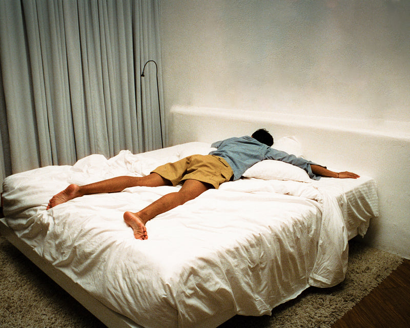 One person lying on a bed in a dimly lit room.