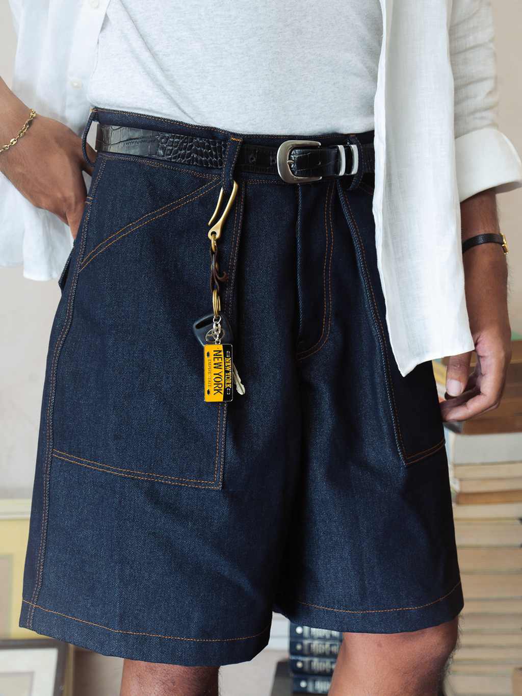Person wearing a white shirt and indigo denim baker shorts with a belt and keychain.