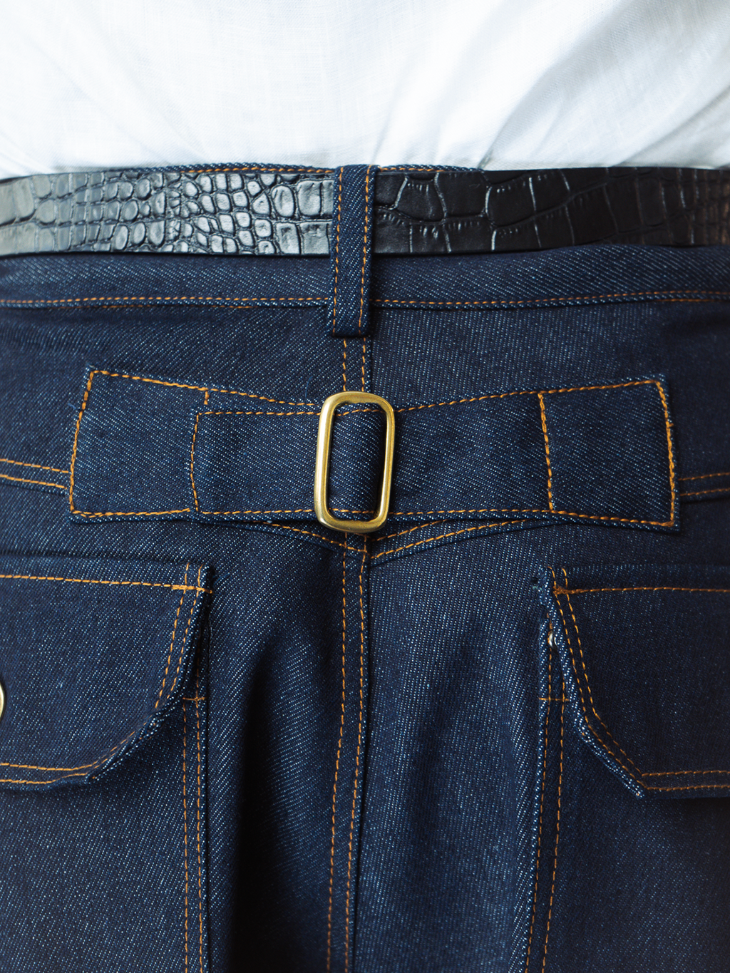 Close-up of indigo denim baker shorts with a gold buckle and white shirt underneath