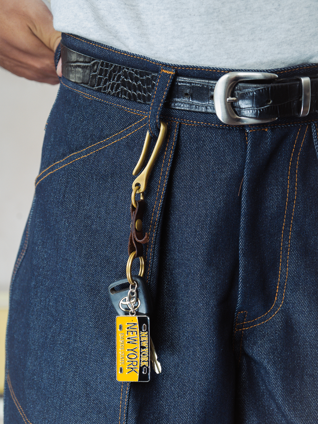 Close-up of indigo denim baker shorts with a keychain attached, featuring a New York-themed tag.