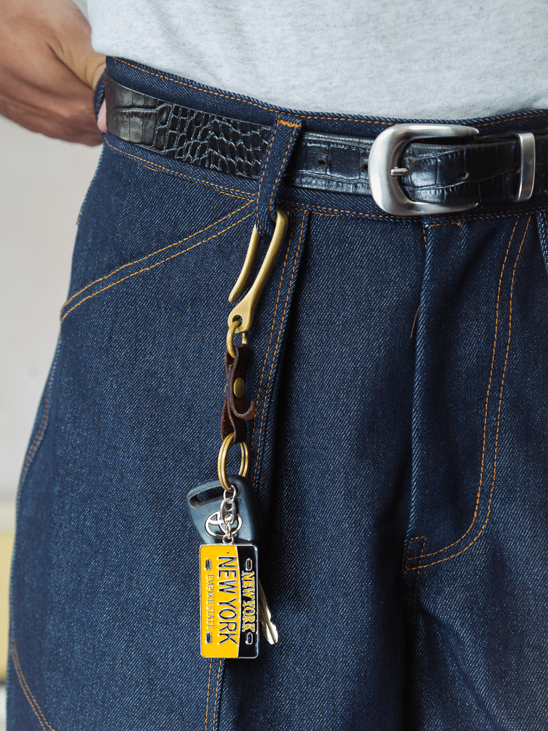 Close-up of indigo denim baker shorts with a keychain attached, featuring a New York-themed tag.