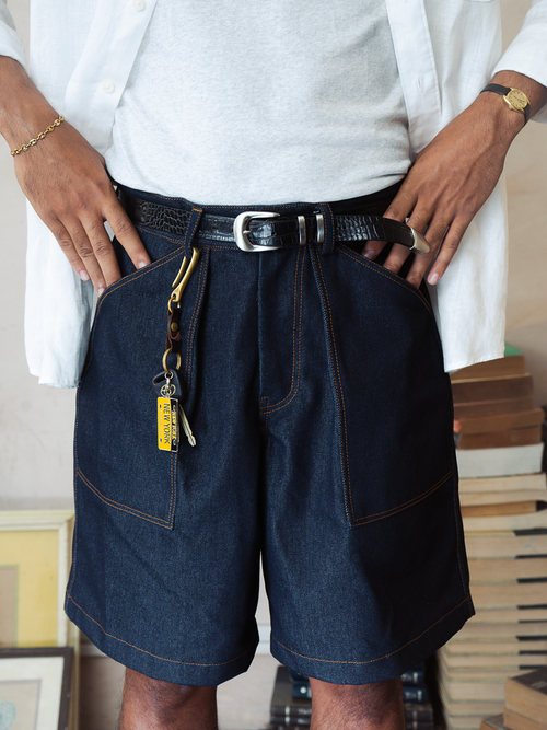 Person wearing dark denim shorts with a belt and keys, standing indoors.