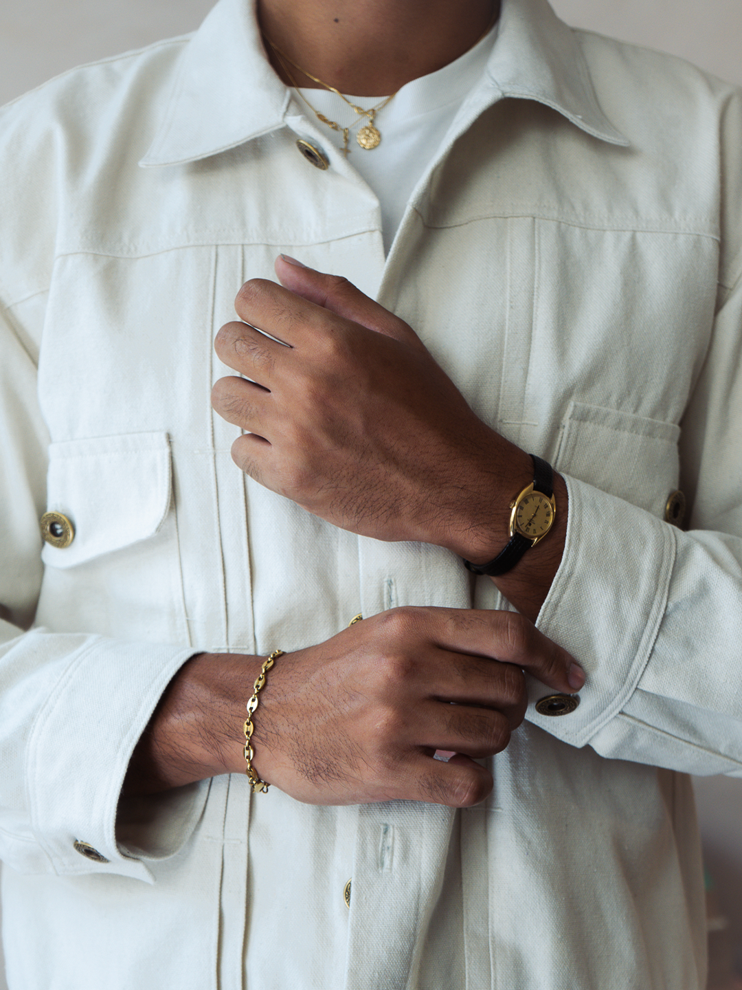 Person wearing a cream type 2 trucker jacket with gold jewelry on a neutral background