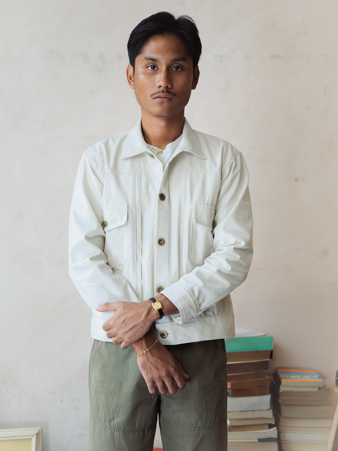 Man wearing a white type 2 trucker jacket with buttons and green pants standing against a neutral wall.