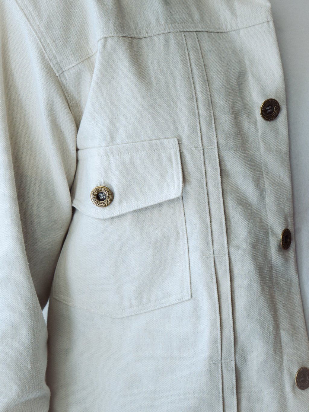 Close-up of a white type 2 trucker jacket with button details on a plain background