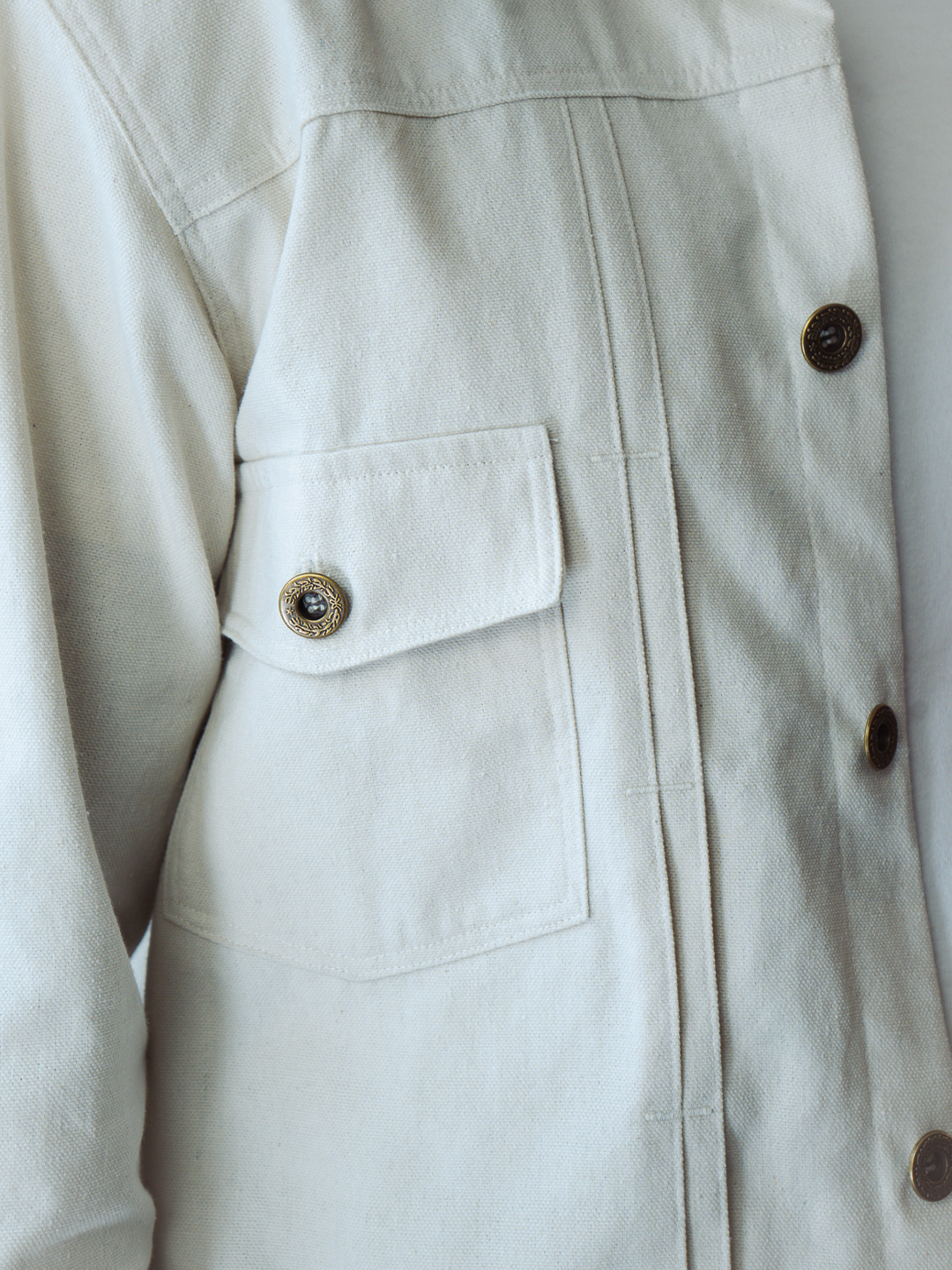 Close-up of a white type 2 trucker jacket with button details on a plain background