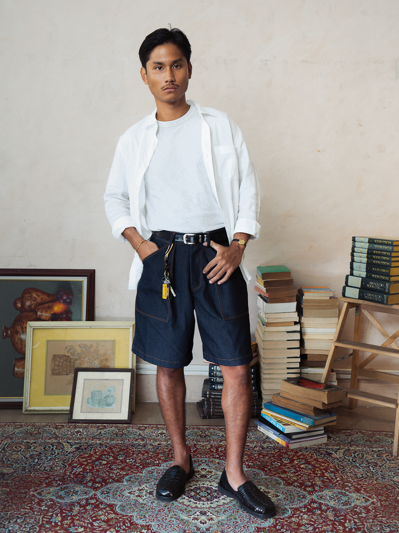 Man in white shirt and tous indigo denim shorts standing in a room with books and artwork.