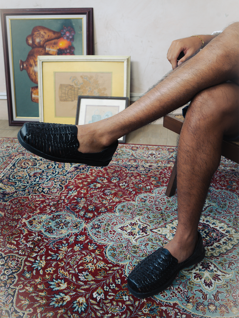 Person wearing black shoes sitting on a patterned rug with framed artwork in the background
