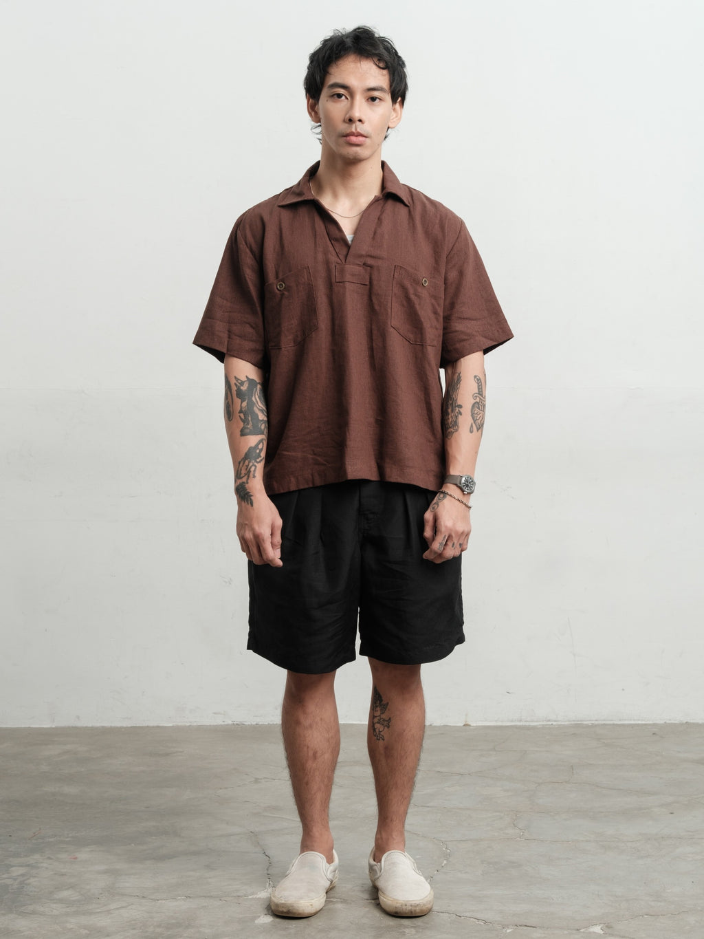 Man wearing a rust brown texture linen smock and black linen gurkha shorts against a white background