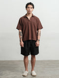Man wearing a rust brown texture linen smock and black linen gurkha shorts against a white background