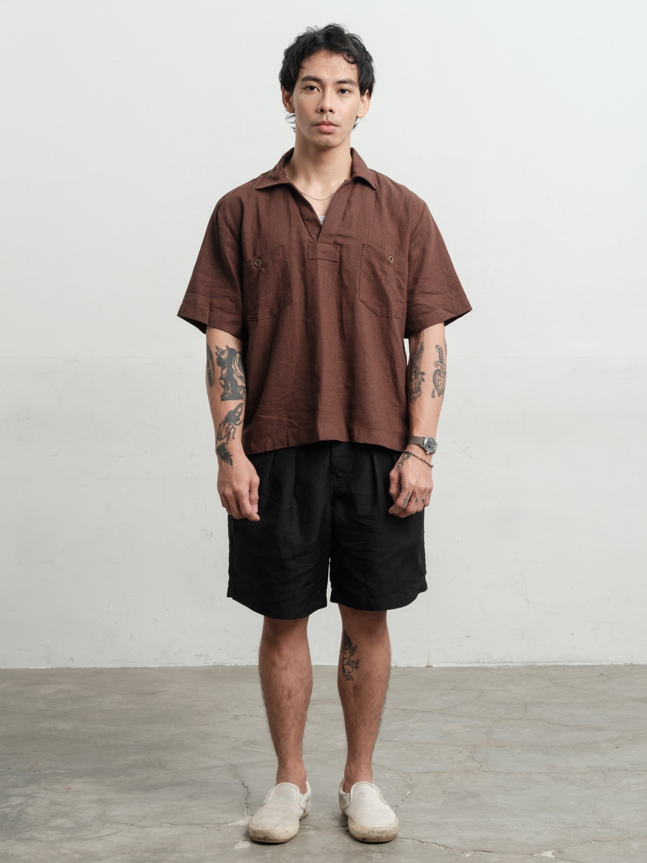 Man wearing a rust brown texture linen smock and black linen gurkha shorts against a white background