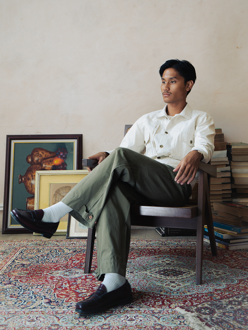 Man sitting on a chair in a room with books and framed pictures.