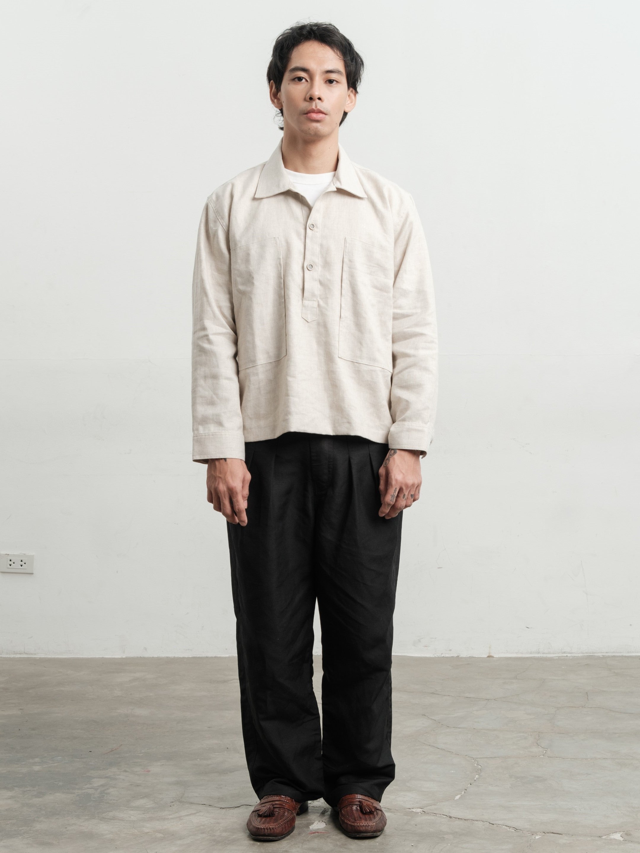 Person wearing a medium weight linen pullover shirt and dark pants against a plain white wall.