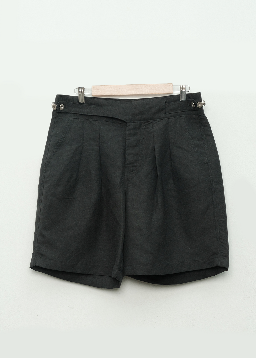 black pleated workwear gurkha shorts on a hanger against a white background