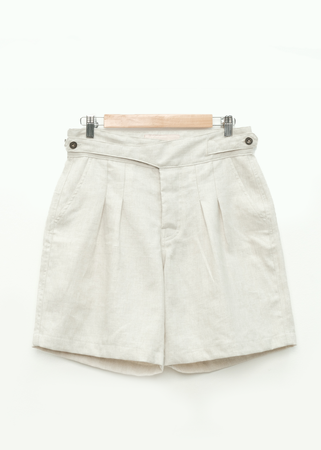 cream pleated workwear gurkha shorts on a hanger against a white background