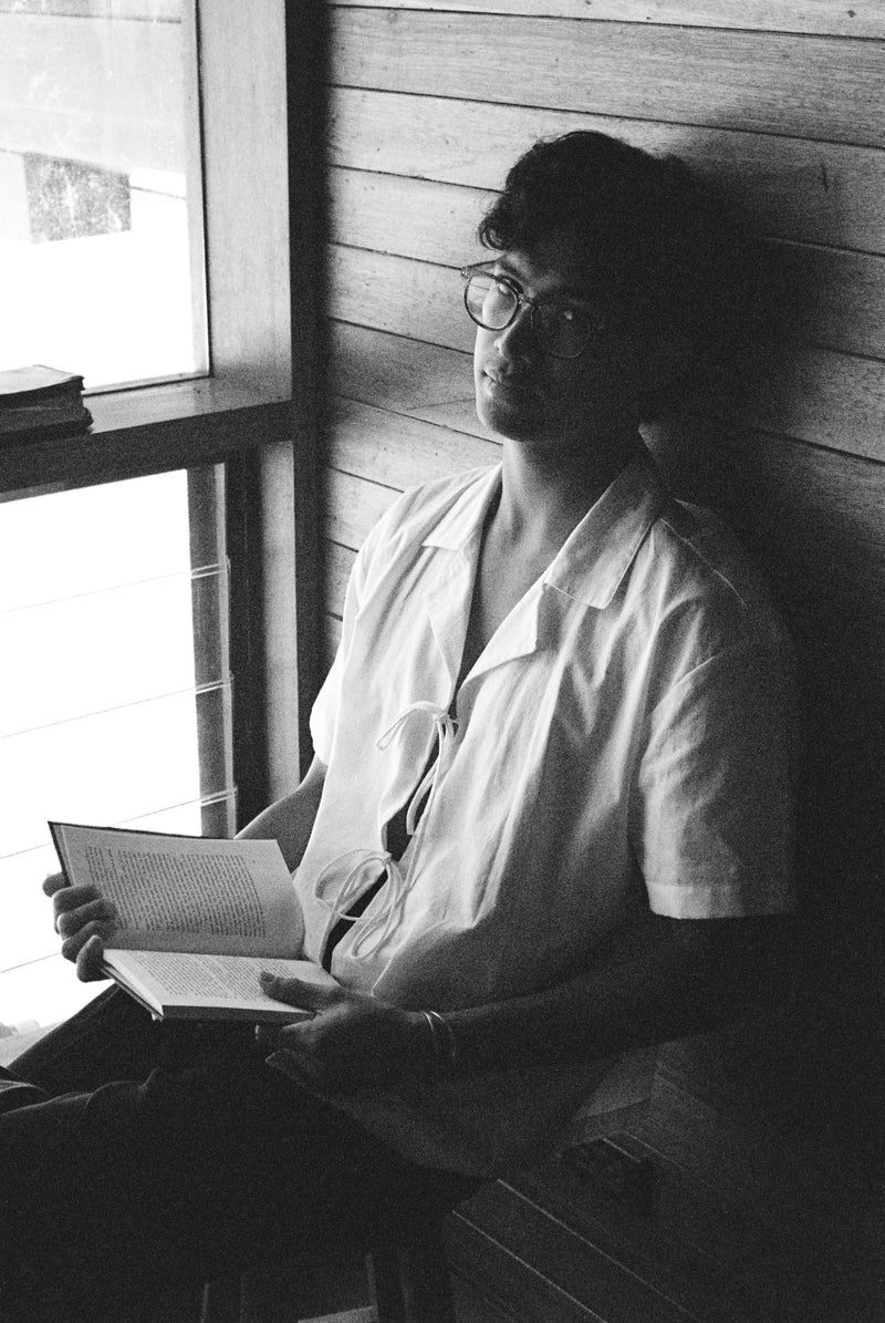 Person sitting by a window reading a book in a room with wooden walls.