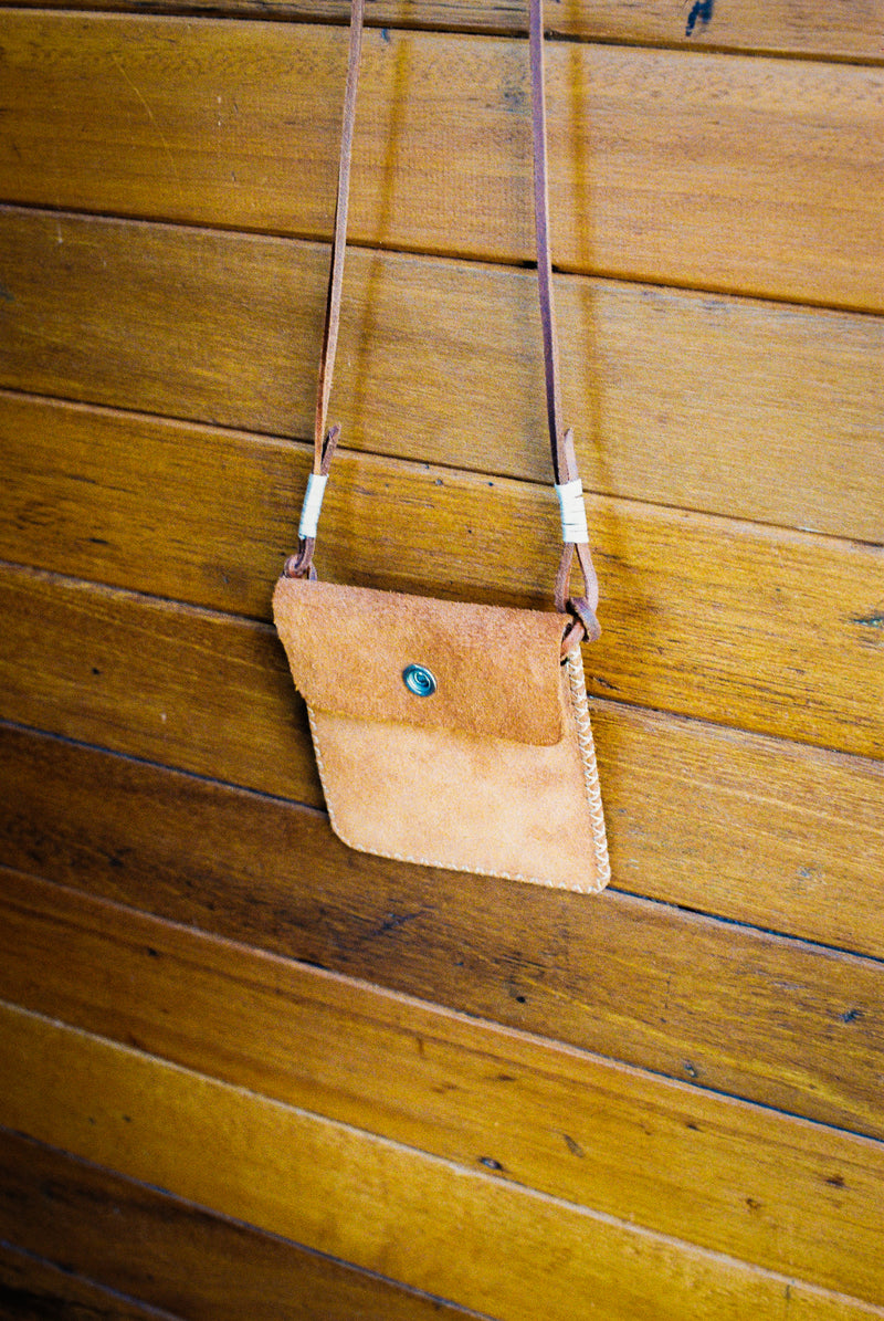 Brown leather crossbody bag with a strap on a wooden surface