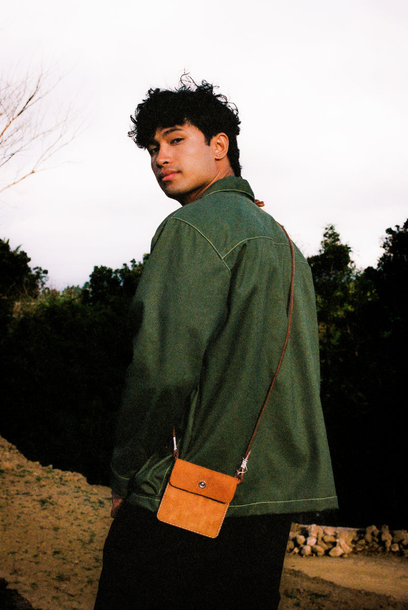 Man wearing a green gardening jacket with a brown leather pouch outdoors