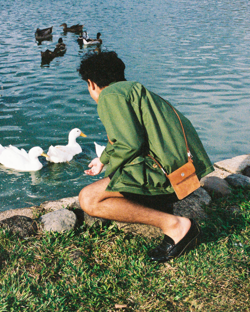 Person in green gardening jacket feeding ducks by a lake