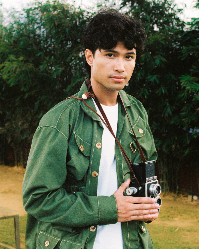 Person wearing a green gardening jacket holding a vintage camera outdoors