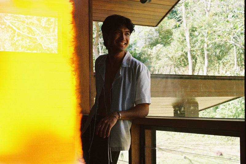 Person standing in a room with large windows, looking out at trees