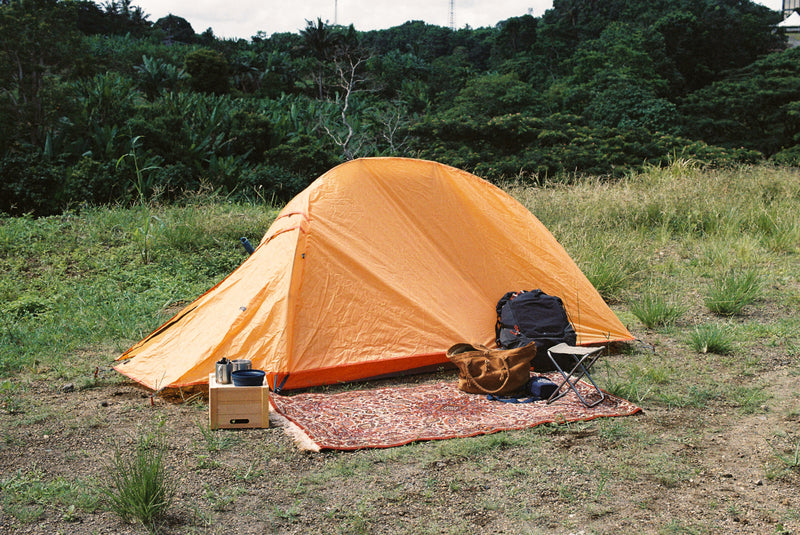 Orange tent set up in a grassy outdoor area with camping gear around.