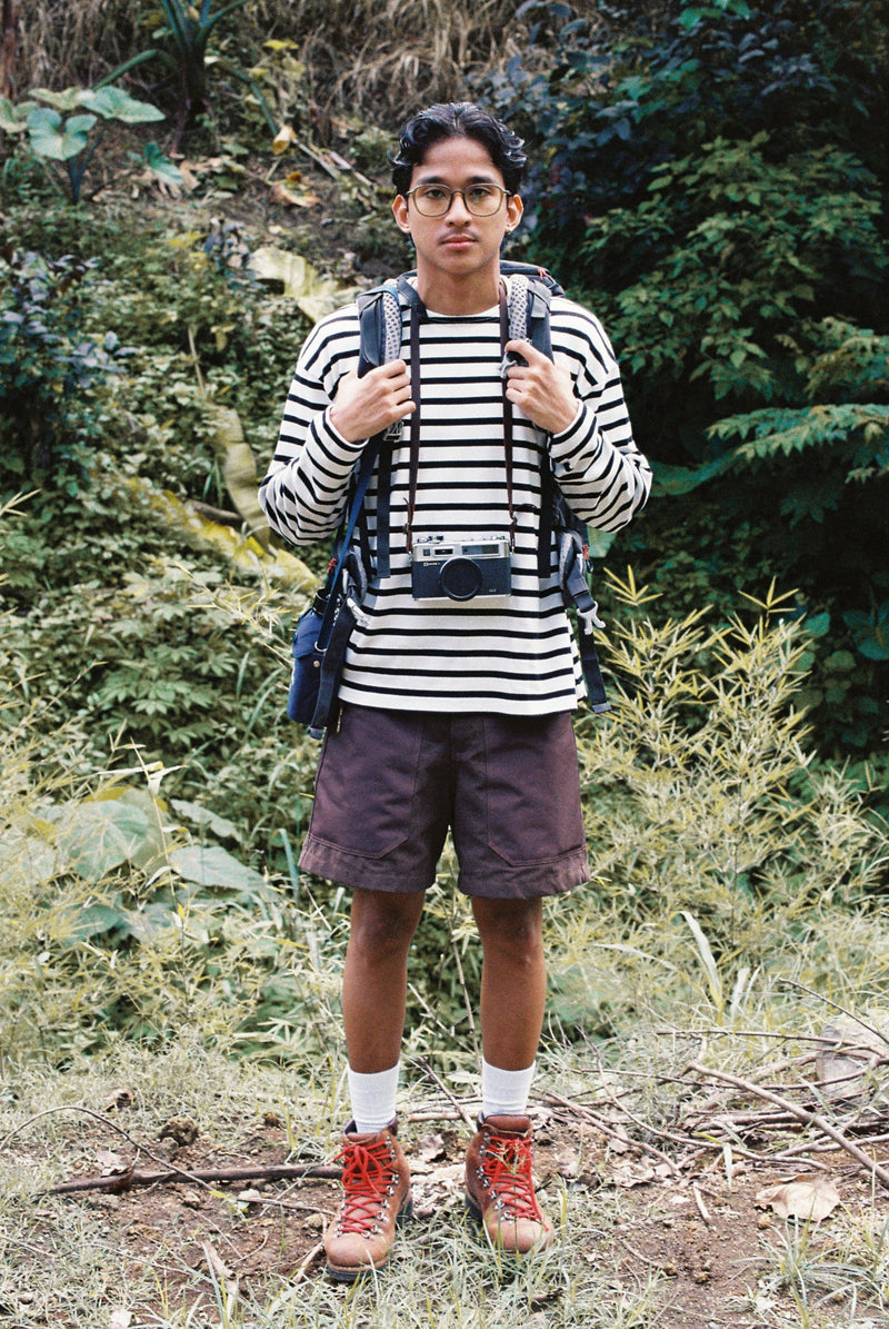 Person wearing a striped shirt and shorts with a backpack in a forest setting