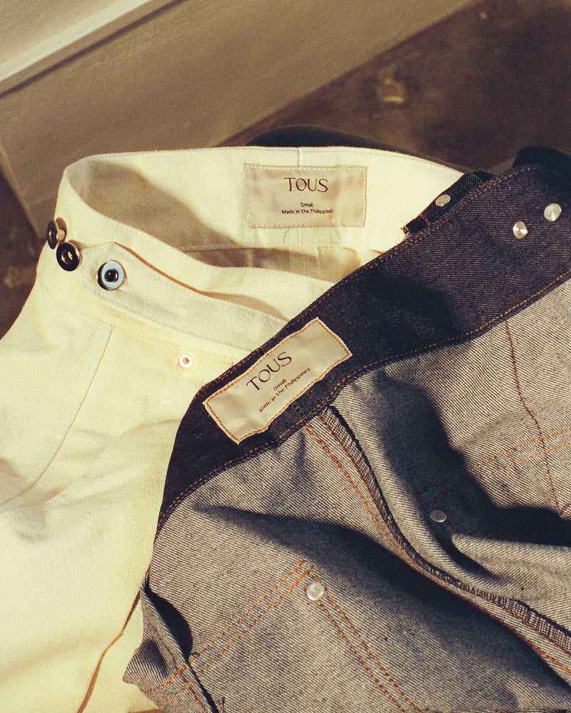 Close-up of denim gurkha pants with 'Tous' labels on a concrete surface.