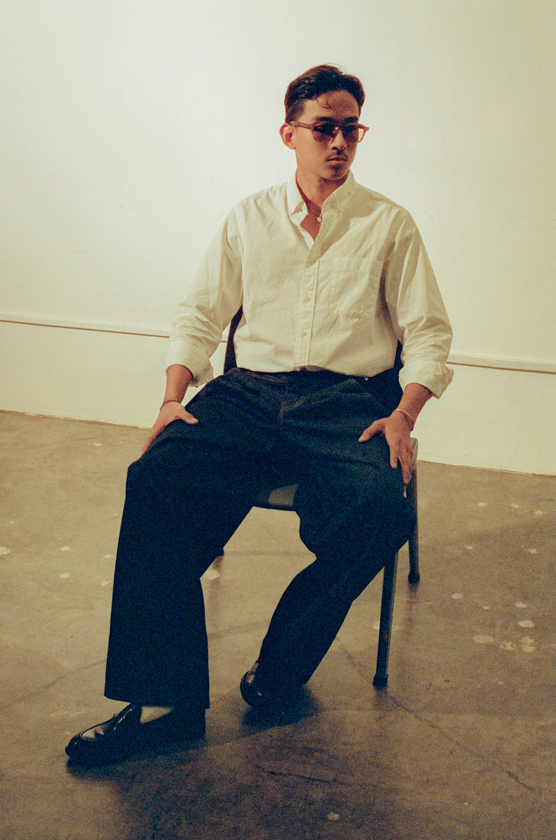 Man sitting on a chair wearing a light-colored shirt and dark pants in an indoor setting.