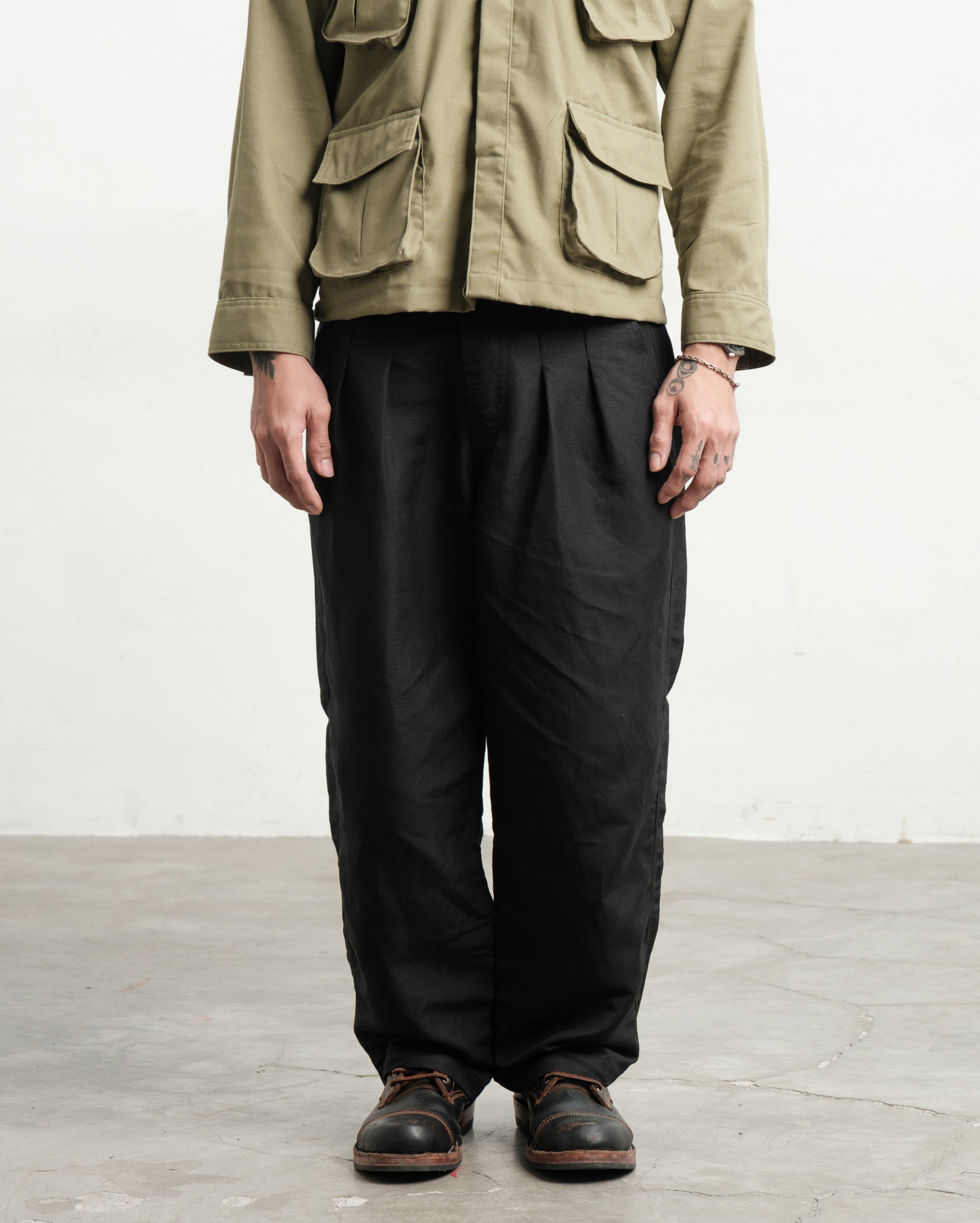 Person wearing a fatigue linen utility workwear jungle jacket and black linen wide legged gurkha pants on a light wooden floor.
