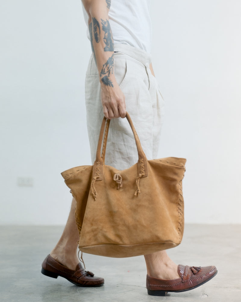 Person holding a brown leather bag against a plain background wearing his tous linen gurkha shorts. 