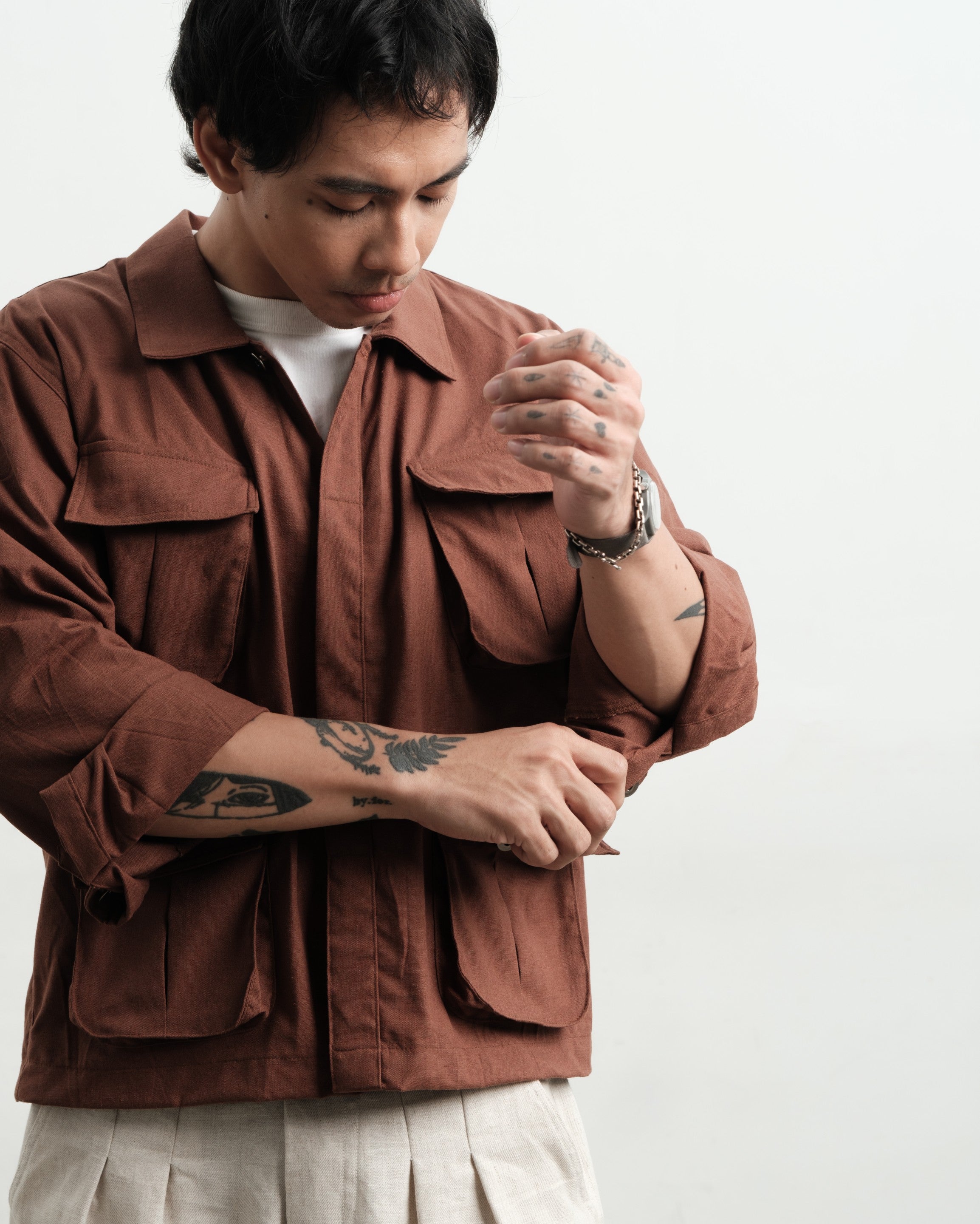Man wearing a brown linen jungle jacket and linen medium weight linen gurkha shorts with tattoos on his arms against a white background