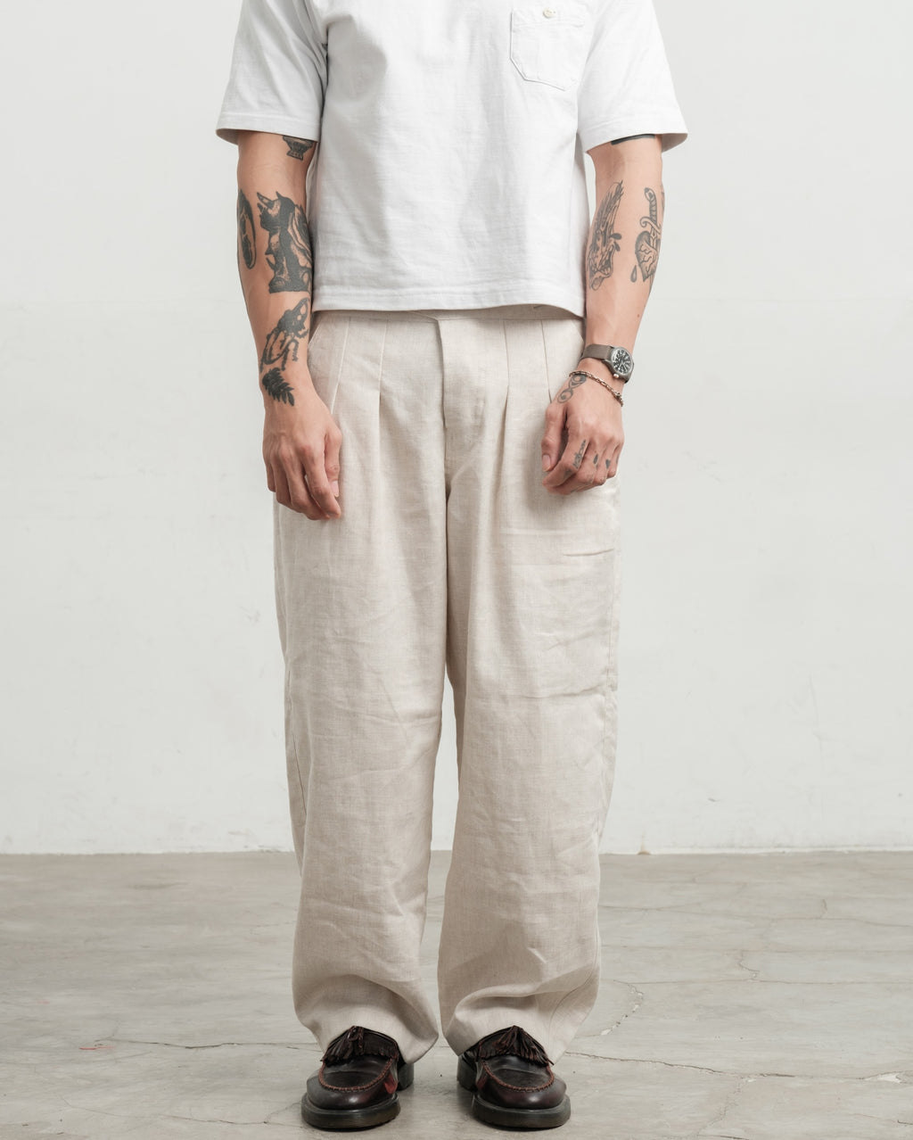 Person wearing a white shirt and cream medium weight wide legged linen gurkha pants against a plain background
