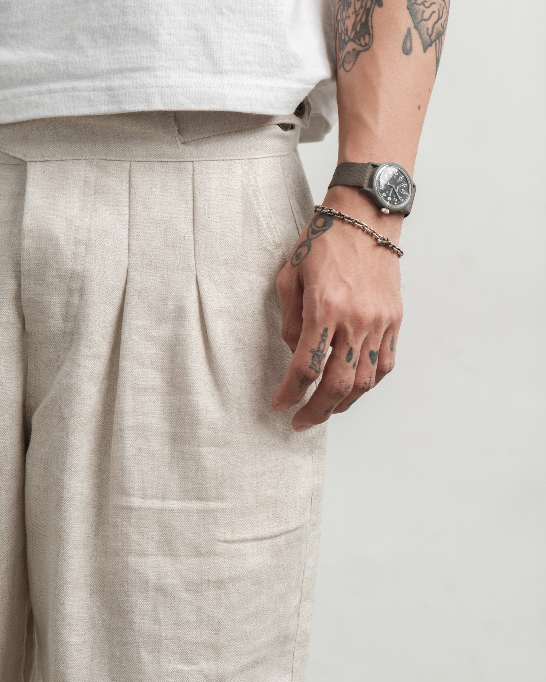 Person wearing cream medium weight wide legged linen gurkha pants and a watch on a plain background