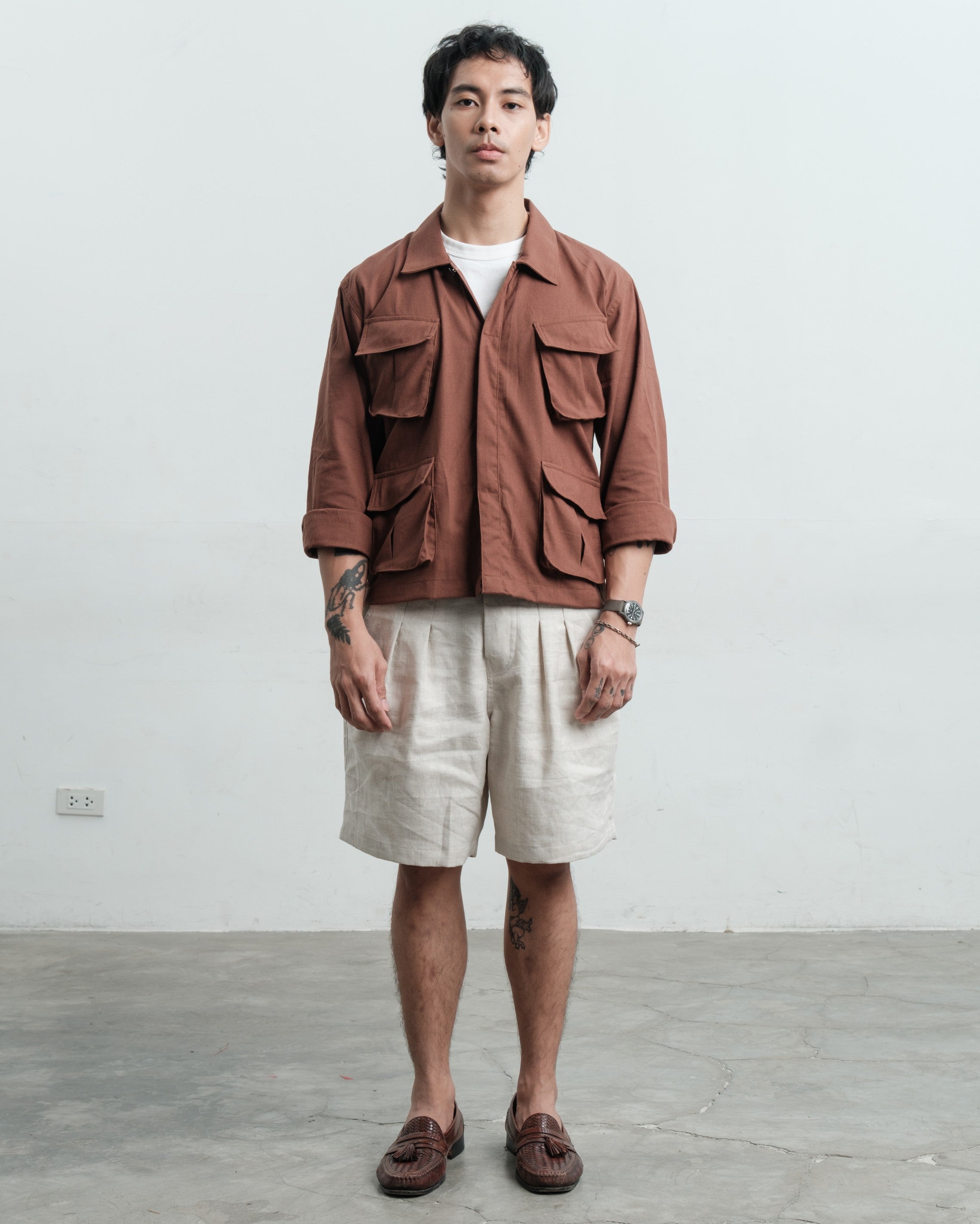 Man wearing a brown linen jungle jacket and linen medium weight linen gurkha shorts against a plain background