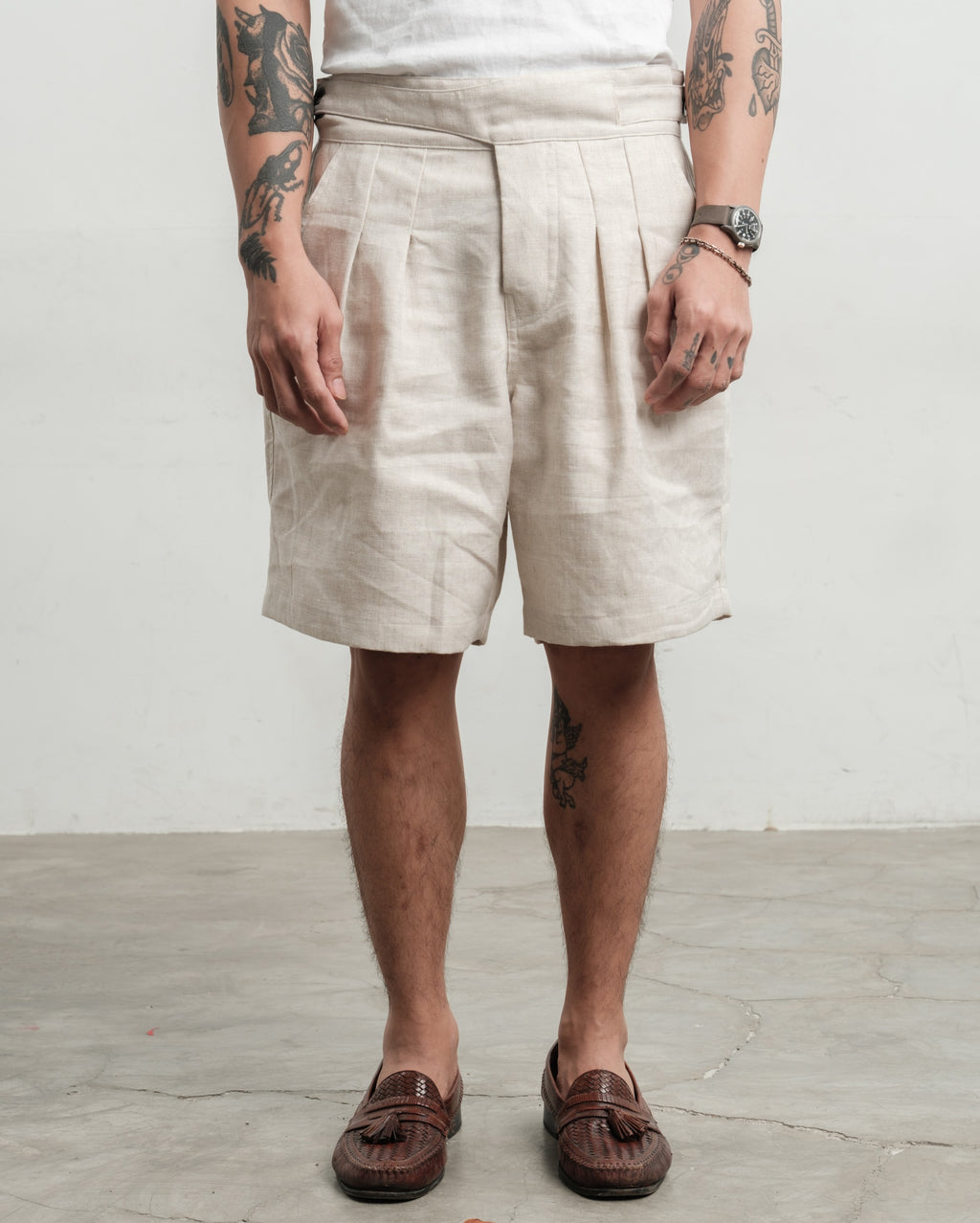 Person wearing cream pleated workwear gurkha shorts with a plain background